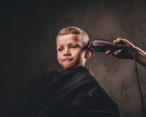 Close-up portrait of a cute preschooler boy getting haircut on a dark background.